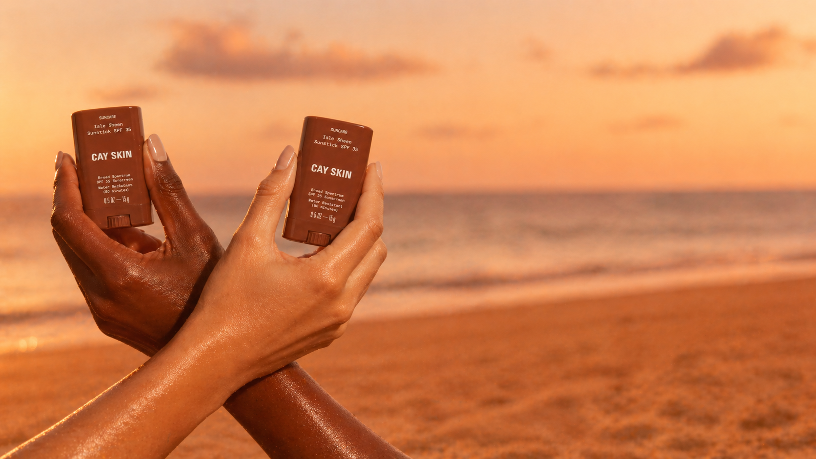 Two Isle Invisible Sunsticks held in melanin-rich hands at golden hour